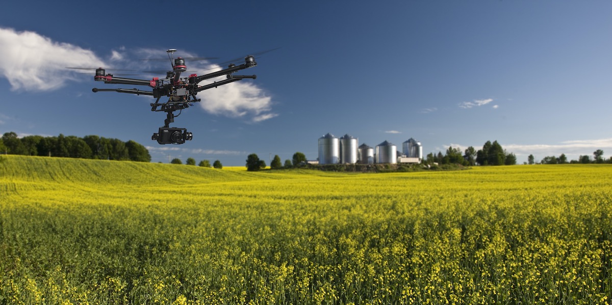 What affects the range of a drone? Image of a drone with a camera flying over an agricultural field.